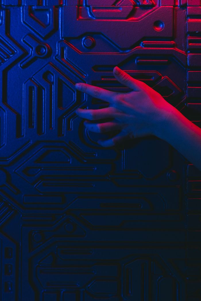 Close-up of a human hand touching a circuit board with blue and red neon lighting.